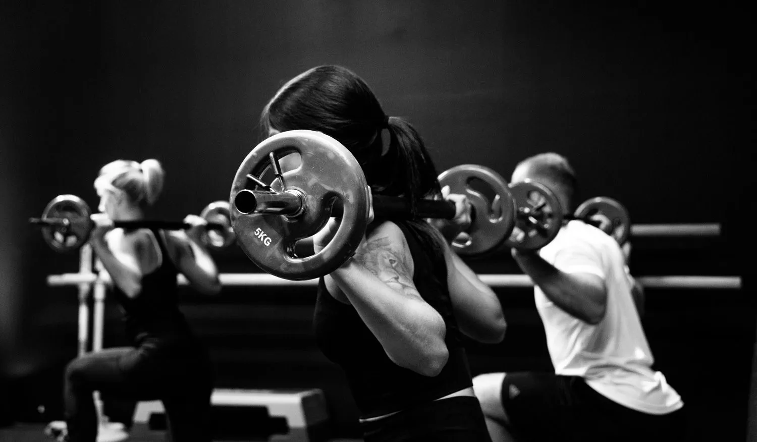 Frau beim Langhanteltraining mit anderen Sportlern