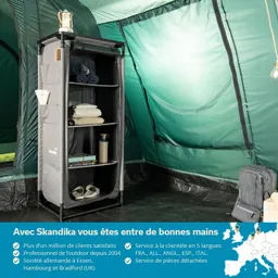 Ein faltbarer Regalschrank steht in einem Zelt, gefüllt mit Handtüchern, Decken und einer Wasserflasche. Ein lanternenförmiges Licht hängt oben.