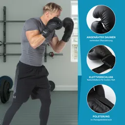Person in Sportkleidung trägt schwarze Boxhandschuhe. Hintergrund mit Fitnessgeräten und einem Fenster.