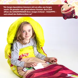 Ein Kind sitzt in einem bunten, gelben Schlafsack. Es hält ein weißes Blatt in der Hand und lächelt. Im Hintergrund ist ein grafisches Element eines cartoonhaften Monsters zu sehen.