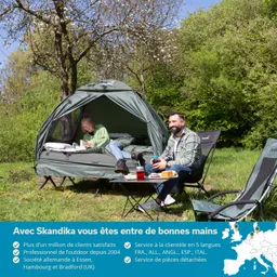 Zelt in der Natur mit zwei Personen. Eine Person sitzt im Zelt und schreibt, die andere entspannt sich draußen. Es gibt einen Tisch mit Snacks und Getränken. Bäume und grünes Gras im Hintergrund.