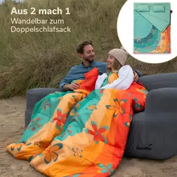 Paar auf einer Couch im Freien, umhüllt von einem bunten Schlafsack mit Blumenmuster. Im Hintergrund Gräser.