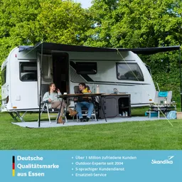 Wohnmobil auf Rasen, zwei Personen an einem Tisch mit Obst und Getränken, Sonnenschutzdach, Bäume im Hintergrund.