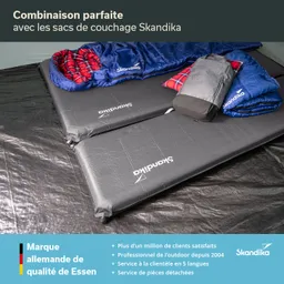 Zwei schwarze Schlafmatten mit dem Logo „Skandika“ liegen nebeneinander. Darauf befinden sich zwei blaue Schlafsäcke und ein Rucksack.