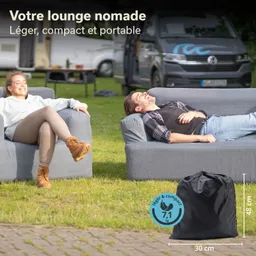 Zwei Personen sitzen entspannt auf grauen Sofas in einem grünen Außenbereich. Ein schwarzer Sack steht auf dem Boden.