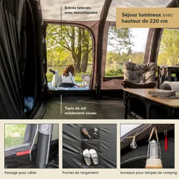Zeltinterieur mit Blick auf eine Wiese. Zu sehen sind eine gemütliche Sitzecke, ein Tisch, Stauraum und ein Bodenbelag mit Kabeldurchführung.
