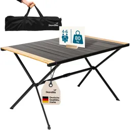 Klappbarer Tisch mit Holzoberfläche, schwarzen Beinen und einer Halterung mit Informationen zu Kapazität und Tragfähigkeit. Tragetasche wird gehalten.