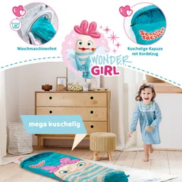 Eine Kinderdecke mit buntem Design liegt auf dem Boden in einem Raum. Eine Person mit kurzen, lockigen Haaren trägt ein blaues Kleid und läuft fröhlich. Im Hintergrund sind eine Kommode und ein Sitzhocker zu sehen.