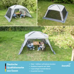 Großes, gestelltes Zelt mit Fenster-Elementen auf einer Wiese. Innen sitzen mehrere Personen um einen Tisch.