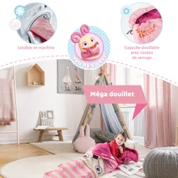 Ein Mädchen liegt in einem Schlafsack mit Tiermotiv in einem hellen Raum. Um sie herum stehen ein Spielzelt, Spielzeug und ein Teppich. Dekorative Elemente wie Kissen sind sichtbar.