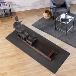 Rudergerät aus schwarzem Kunststoff und Holz auf einem dunklen Unterlageteppich. Im Hintergrund ein Sessel und ein Couchtisch.