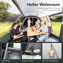 Campingzelt mit Sitzgelegenheiten und Tisch, umgeben von Menschen. Helle Innenausstattung, Sicht auf Natur.