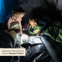 Zwei Kinder sitzen in einem Zelt, beleuchtet von einer Taschenlampe. Sie betrachten ein aufgeschlagenes Buch.