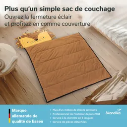 Schlafsack in Form eines Löwenkopfes auf Holzfußboden, daneben Stellfläche mit einem Kissen und Decke.