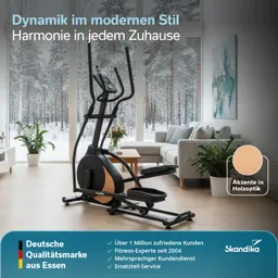 Ein Crosstrainer steht in einem modernen Wohnzimmer mit großen Fenstern und Blick auf einen verschneiten Wald. Couch und Pflanzen sind ebenfalls sichtbar.