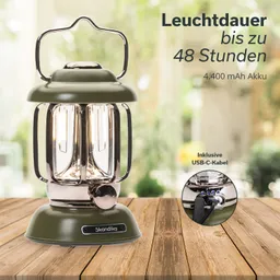 Grüne Laterne mit zwei Glühbirnen und einem stabilen Standfuß, auf einem Holztisch platziert. Hintergrund unscharf.