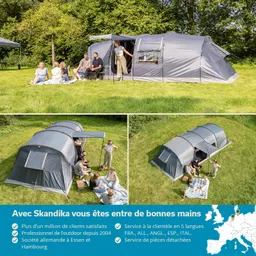 Zwei Zelte auf einer grünen Wiese, umgeben von Bäumen. Personen sitzen und liegen auf einer Decke, einige unterhalten sich.