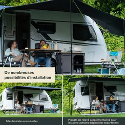 Caravan mit offenem Vorbau, zwei Personen sitzen an einem Tisch, Obst und Getränke sind sichtbar. Umgeben von Bäumen.