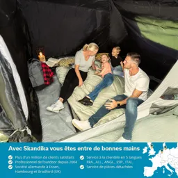 Familie sitzt in einem Zelt auf einer Schlafunterlage. Zwei Erwachsene und zwei Kinder lachen und interagieren. Ein Rucksack und eine Laterne sind sichtbar.