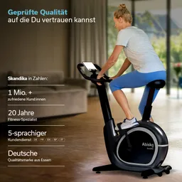 Ein Mann sitzt auf einem schwarzen Heimtrainer und betrachtet einen Bildschirm. Der Raum ist hell und modern eingerichtet.