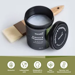 Ein schwarzer Behälter mit Pflegepaste steht neben einem Pinsel. Die Dose ist geöffnet, die Paste ist sichtbar. Unter dem Behälter sind fünf grüne Symbole mit Text.