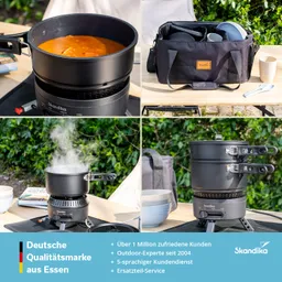 Kocher mit einem Topf, in dem eine Suppe kocht. Neben dem Kocher eine Tasche mit Geschirr und Besteck. Grüne Pflanzen im Hintergrund.