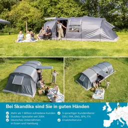 Großes graues Zelt auf einer Wiese, eine Gruppe von Menschen sitzt und steht in der Nähe, darunter einige auf einer Decke.