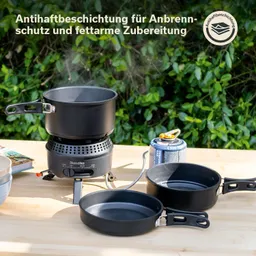 Einfache Campingkochausrüstung auf einem Tisch: ein Topf, zwei Pfannen, ein Gaskartuschenbrenner und eine grüne Umgebung.