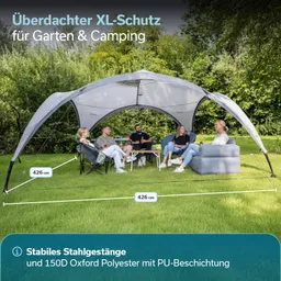 Überdachte Sitzgelegenheit mit einem großen, grauen Sonnenschutz. Vier Personen sitzen um einen Tisch auf einer Wiese.