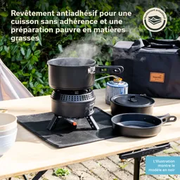 Kochausrüstung auf einem Tisch: Ein schwarz beschichteter Kochtopf mit Dampf, auf einem Gaskocher, umgeben von weiteren Küchenutensilien und einem Rucksack.