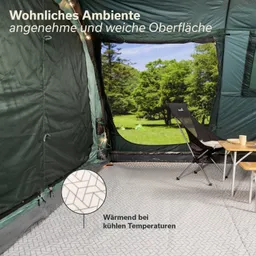 Innenraum eines Zeltes mit grauem, gemustertem Boden, einem Stuhl und einem Tisch. Fenster zeigt grünes Außen, Bäume sichtbar.