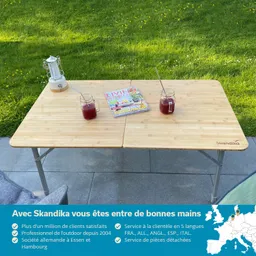 Tisch aus Holz mit zwei Gläsern, einer Zeitschrift und einer Laterne auf grünem Rasen im Hintergrund.