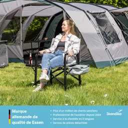 Eine Person sitzt entspannt in einem Gartenstuhl vor einem Zelt auf einer Wiese.