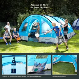 Zelt in Blau und Grau mit flexiblen Fiberglasstangen, umgeben von Personen auf einer Wiese. Zubehör wie Lampe und Fächer sichtbar.