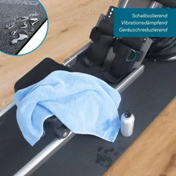 Fitnessgerät mit einem Handtuch und einer Wasserflasche. Der Boden ist hellbraun, das Gerät hat schwarze und graue Elemente.