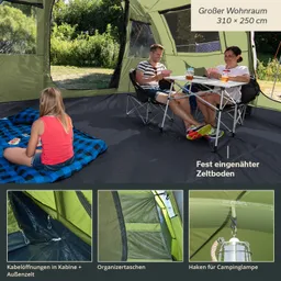Zeltinnenraum mit zwei Personen am Tisch, eine Person sitzt auf einer Decke und spielt Karten. Zeltboden und Fenster sichtbar.
