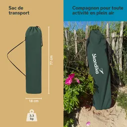 Grüner Transportbeutel steht auf Sand, mit Maßangaben und Logo „Skandika“. Im Hintergrund Pflanzen und Zaun sichtbar.