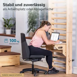 Eine sitzende Person schreibt an einem Tisch, umgeben von Pflanzen. Der Tisch ist aus Holz und hat eine Ablagefläche.