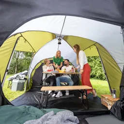 Vier Personen sitzen und stehen in einem Zelt. Ein Tisch ist mit Snacks und Getränken gedeckt. Im Hintergrund ist ein Müllbehälter und eine Gruppenjacke sichtbar.