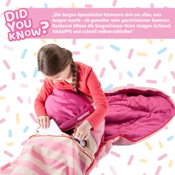 Ein Kind sitzt in einem Schlafsack mit pinken Streifen und öffnet eine Tasche mit bunten Gegenständen. Der Hintergrund ist mit bunten Streuseln gestaltet.