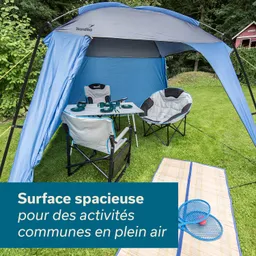 Blaues Zelt mit einem Tisch und zwei Stühlen auf einer Wiese, daneben eine Decke und zwei Spielgeräte.