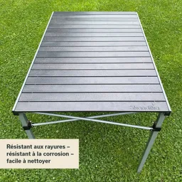 Ein klappbarer Tisch mit einer schwarzen Oberplatte und silbernen Beinen steht auf grünem Gras.