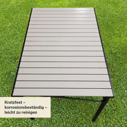 Ein grauer Tisch mit horizontalen Laminatleisten auf grünem Gras. Links unten steht ein Schild mit Produktinformationen.