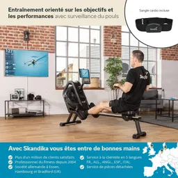 Person auf einem Rudergerät in einem modern eingerichteten Raum. An der Wand ein Bildschirm mit Trainingsdaten. Möbel im Hintergrund sichtbar.