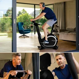 Eine Person trainiert auf einem schwarzen Heimtrainer in einem modernen Raum mit großen Fenstern. Im Hintergrund sind ein blauer Sessel und Pflanzen sichtbar.