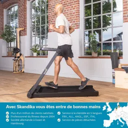 Mann joggt auf einem Laufband in einem hellen Raum mit großen Fenstern und Holzfußboden. Pflanzen sind sichtbar.