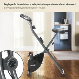 Faltbares Exercycle mit einem Sitz, einem drehbaren Widerstandsknopf und einem schwarzen Gehäuse. Helle Inneneinrichtung im Hintergrund.