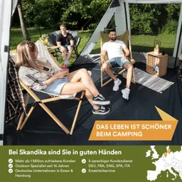 Drei Personen sitzen in Campingstühlen in einem Zelt. Ein Tisch mit Getränken steht in der Mitte. Grüne Bäume im Hintergrund.