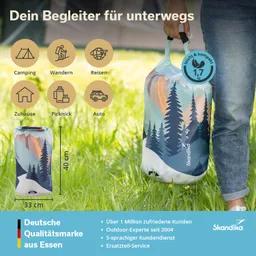 Kompakte Tasche mit buntem Landschaftsmuster, getragen von einer Person in Jeans, auf einer Wiese.