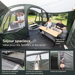 Geräumiges Zelt mit Sitzecke und Tisch. Zwei Personen sitzen entspannt, während eine Person am Grill arbeitet.